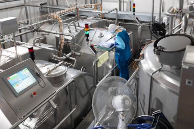 Mavi cüppeli ve şapkalı işçiler süt fabrikasının üretim departmanını teftiş ediyor.