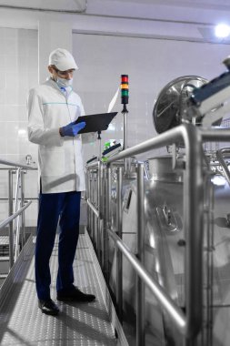 Bir maske ve bir scrub müfettiş elinde bir klasör-tablet ile süt fabrikasında duruyor