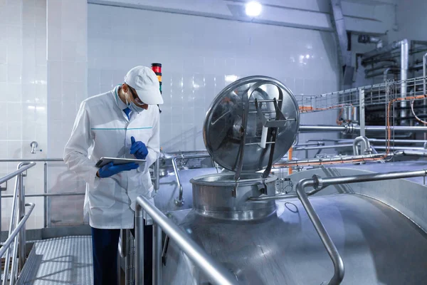 Ispettore con una maschera e uno scrub in piedi con una cartella-tablet tra le mani presso lo stabilimento lattiero-caseario — Foto Stock