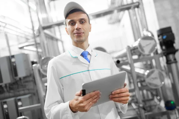 Retrato del hombre con una bata blanca y una gorra de pie en el departamento de producción de la fábrica de lácteos con tabletas grises — Foto de Stock