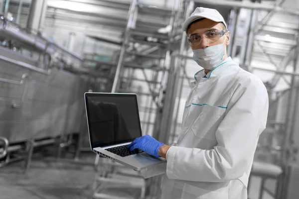 Retrato do homem com um manto branco e uma tampa em pé no departamento de produção da fábrica de laticínios com tablet cinza — Fotografia de Stock