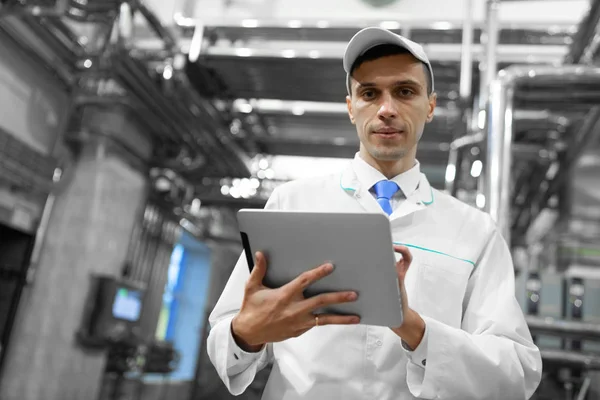 Retrato del hombre con una bata blanca y una gorra de pie en el departamento de producción de la fábrica de lácteos con tabletas grises — Foto de Stock