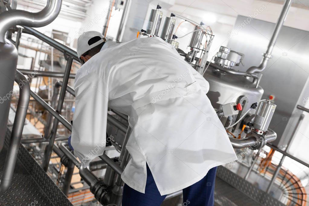 worker in a blue robe and a cap inspect the production department of dairy factory