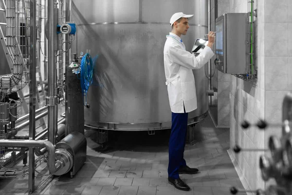 Porträtt av mannen i en vit mantel och en mössa stående i produktionsavdelningen av mejeri fabriken med laptop — Stockfoto
