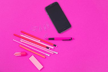 Pembe ofis ekipmanları ve bir siyah cep telefonu izole pembe arka plan üzerinde yatıyor