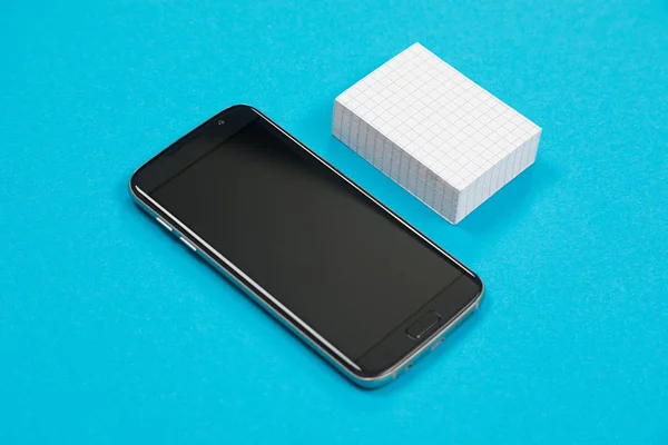 Černý mobilní telefon a hromada bílého papíru leží na azurové ploše izolované Royalty Free Stock Fotografie
