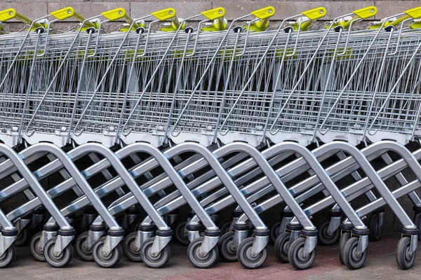 Many gray steel shopping trolleys with yellow handles standing in a row as background for shopping news topics. Stands, wheels lower part, bottom part of trolleys are crossed and make up diagonal