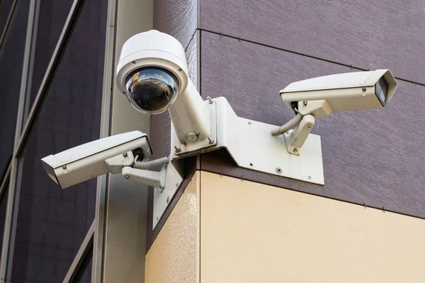 Vista inferior de três câmeras de vigilância brancas no prédio de escritórios com parede de azulejos maroon amarelo pálido e pálido — Fotografia de Stock