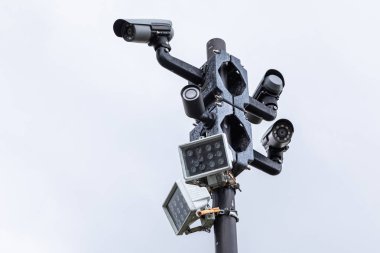 Beyaz gökyüzüne karşı sütun üzerinde siyah cctv izleme kameraları ve sokak lambaları yakın çekim