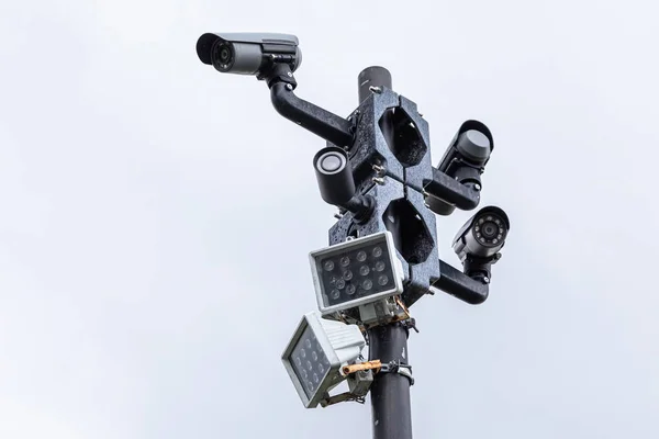 Крупним планом чорні камери спостереження та вуличні ліхтарі на колонці проти білого неба — стокове фото