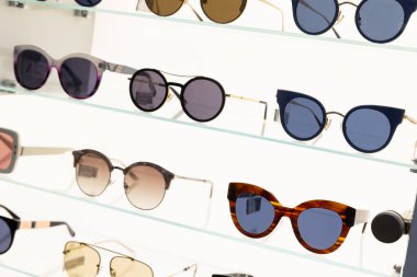 Many sunglasses of different shape on shopping centre shelves on white shiny background.