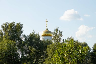 Ağaçların yeşil tepeleriyle çevrili beyaz doğu kilisesinin altın kubbesi.