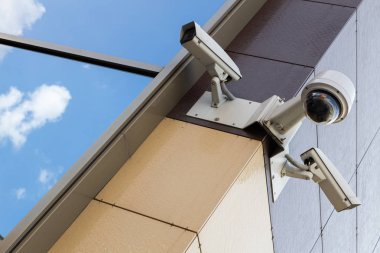Diagonal ground view of three white surveillance cameras on office building with glass wall