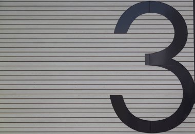 Büyük siyah üç numara gri ahşap duvarda.