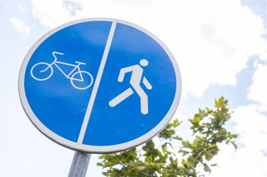 Yol işaretine yakın bisiklet sürücüleri ve yayalar için güneşli gökyüzüne karşı paylaşılan yol