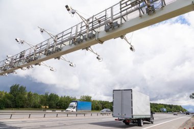 Bulutlu gökyüzü ve ormanın karşısında yol ayrımında beyaz bir kamyonet var.