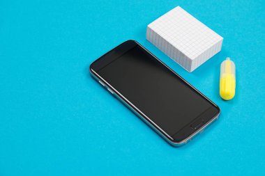 Siyah cep telefonu, post-it yığını ve mavi arka planda sarı bir işaret.