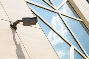 Figürlü pencerede gökyüzü yansıması ile bej döşenmiş duvar yüzeyinde güvenlik kamerası zemin çapraz görünümü.