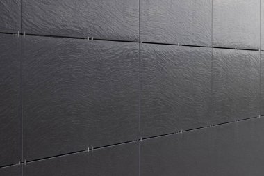 Yapı duvarının parlak siyah yüzeyi ve birbirine bağlı fayanslar. Alanın derinliğine sahip fotoğraf