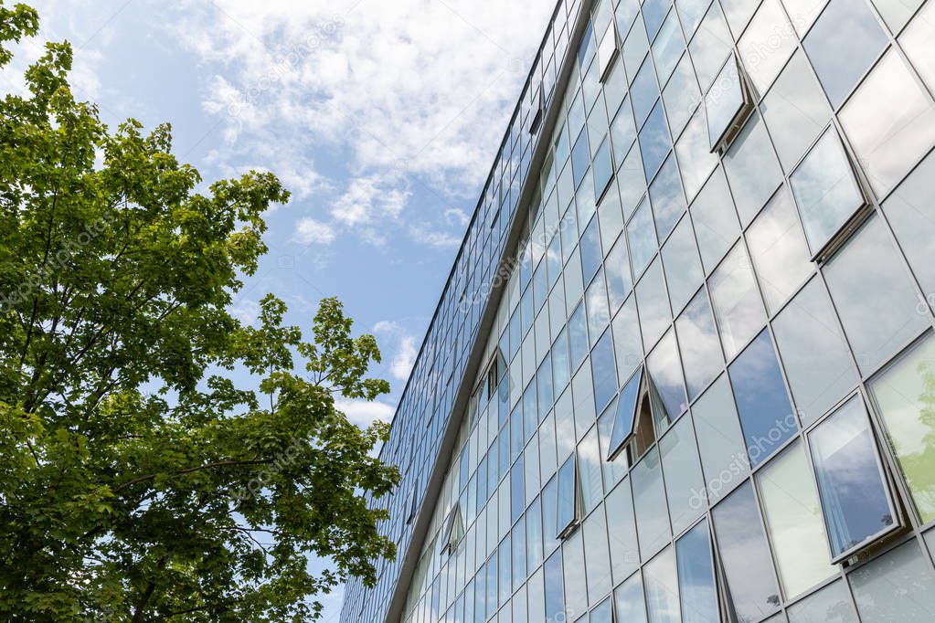 Modern building with glass reflecting facade co-existing with sky background and tree.