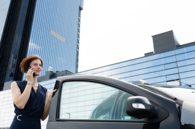 Güzel bir kadın arabanın yanında telefonla konuşuyor. 