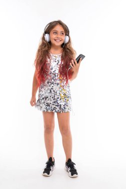 Güzel bir kız, kulaklık ve cep telefonuyla beyaz arka planda poz veriyor.