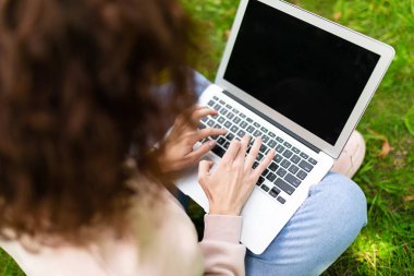 Kız laptopla çalışıyor çimlerin üzerinde oturuyor. 