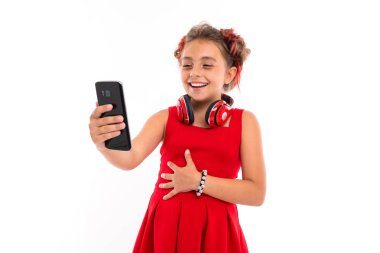 Beyaz arka planda cep telefonuyla poz veren sevimli küçük kız.  