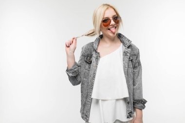 Arka planda güneş gözlüğü takan, kot ceketli neşeli, sarışın kızın portresi.
