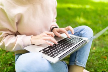 Kız laptopla çalışıyor çimlerin üzerinde oturuyor. 