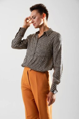 Çizgili siyah beyaz gömlekli, turuncu pantolonlu güzel bir kadın stüdyoda poz veriyor. 