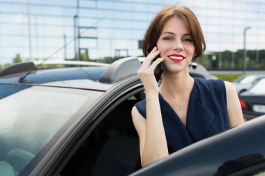 Güzel bir kadın arabanın yanında telefonla konuşuyor. 