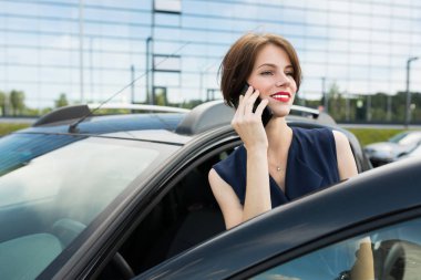 Güzel bir kadın arabanın yanında telefonla konuşuyor. 
