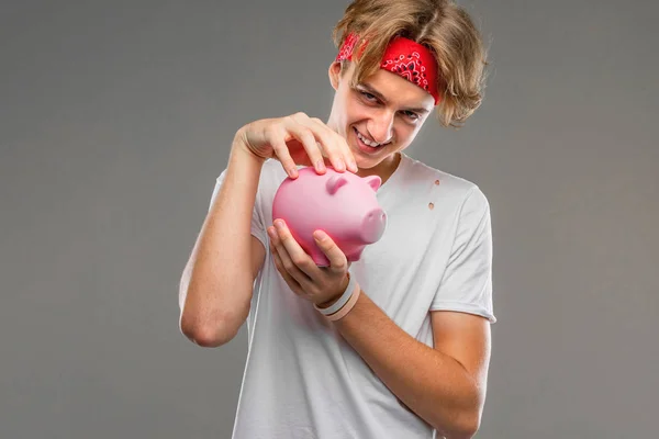 teenager with piggy bank posing against gray