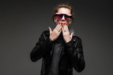 Deri ceketli ve gri gözlükle poz veren zarif genç bir kadın. 