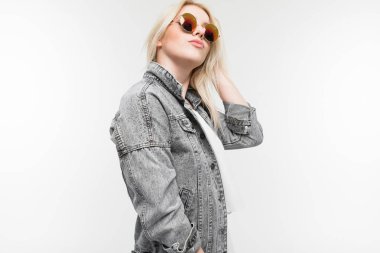 Arka planda güneş gözlüğü takan, kot ceketli neşeli, sarışın kızın portresi.