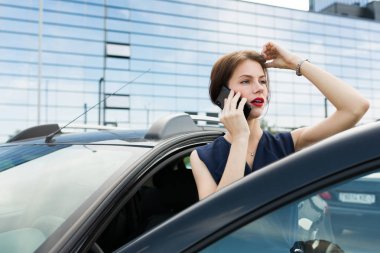 Güzel bir kadın arabanın yanında telefonla konuşuyor. 
