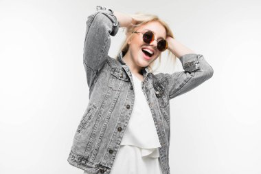 Arka planda güneş gözlüğü takan, kot ceketli neşeli, sarışın kızın portresi.