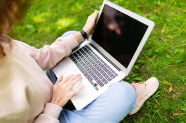 Kız laptopla çalışıyor çimlerin üzerinde oturuyor. 
