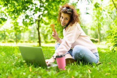 Kadın dondurma yerken dizüstü bilgisayarda çalışıyor.