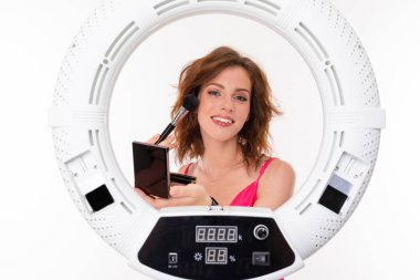 Genç bir kadın aynaya makyaj yapıyor. 