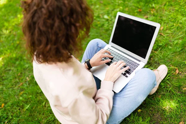 Kız laptopla çalışıyor çimlerin üzerinde oturuyor. 