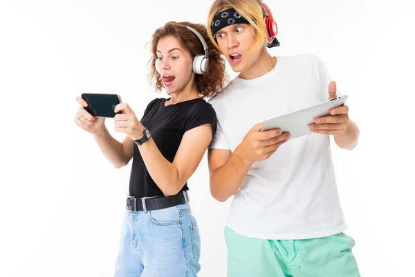 Woman with mobile phone and man with digital tablet posing in headphones against white background