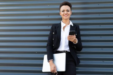 Telefonlu ve bilgisayarlı güzel bir iş kadınının açık hava portresi.