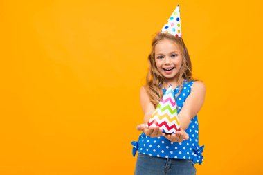 Küçük akıllı kız turuncu arka planda hediyeyle poz veriyor.  