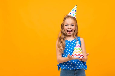 Küçük akıllı kız turuncu arka planda hediyeyle poz veriyor.  