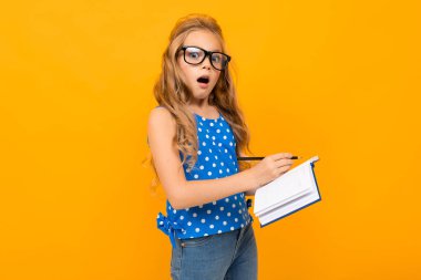 Gözlük ve defterle turuncu arka planda poz veren küçük akıllı kız.  