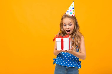 Küçük akıllı kız turuncu arka planda hediyeyle poz veriyor.  