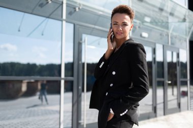 Güzel bir iş kadını dışarıda telefonla poz veriyor.