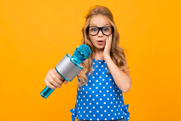 милая маленькая девочка с микрофоном позирует против оранжевого
